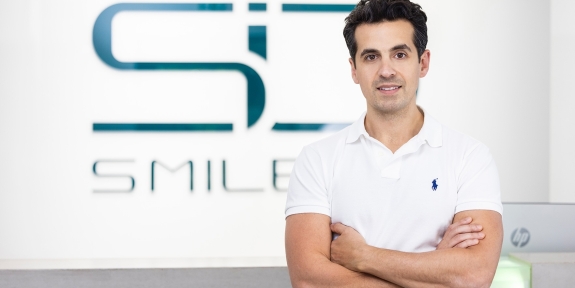 Dr. Assadi steht selbstbewusst vor dem SMILE ID-Logo